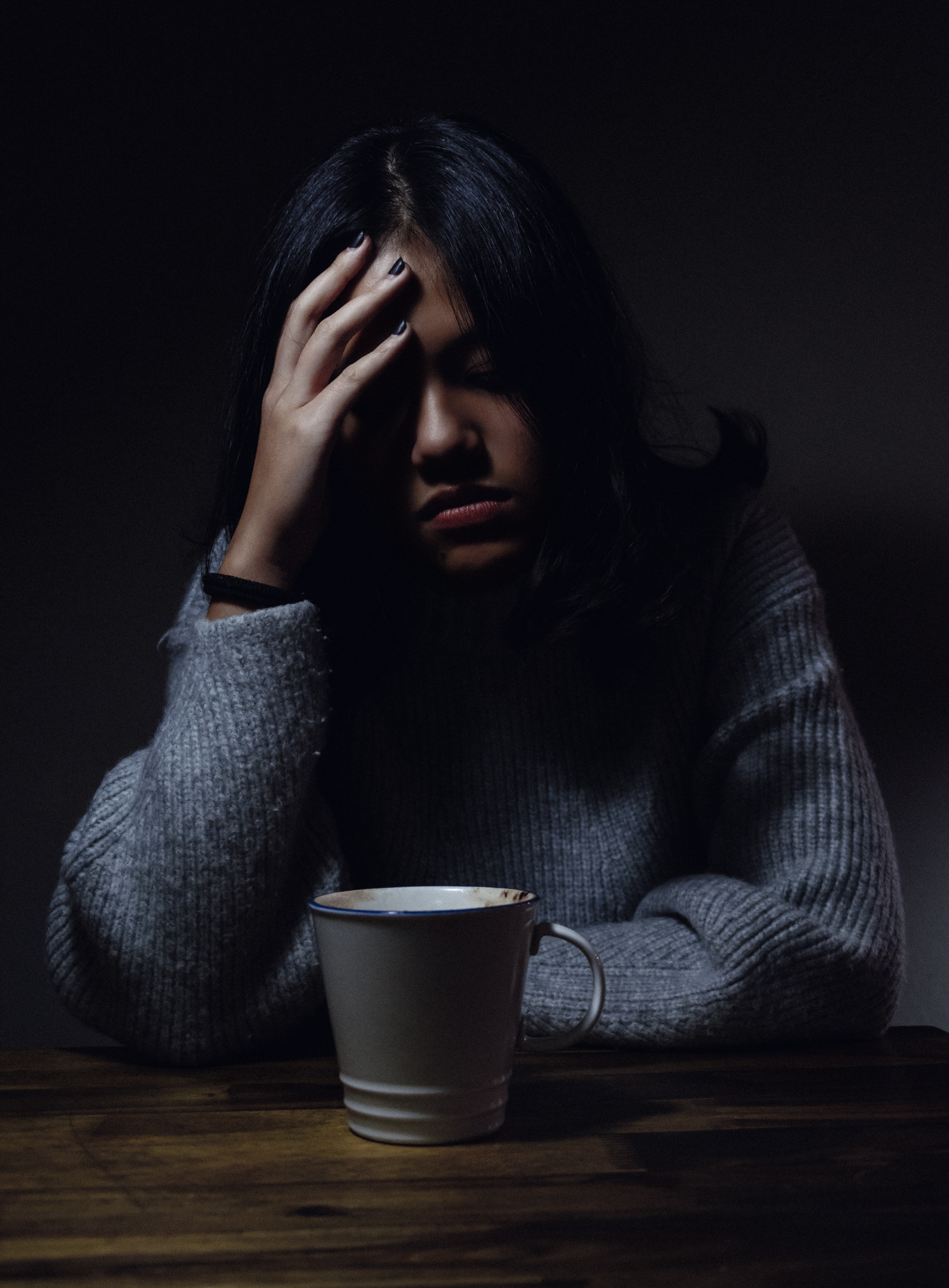Treatment Resistant depression: a woman sitting in a darkened room with one hand on the side of her head